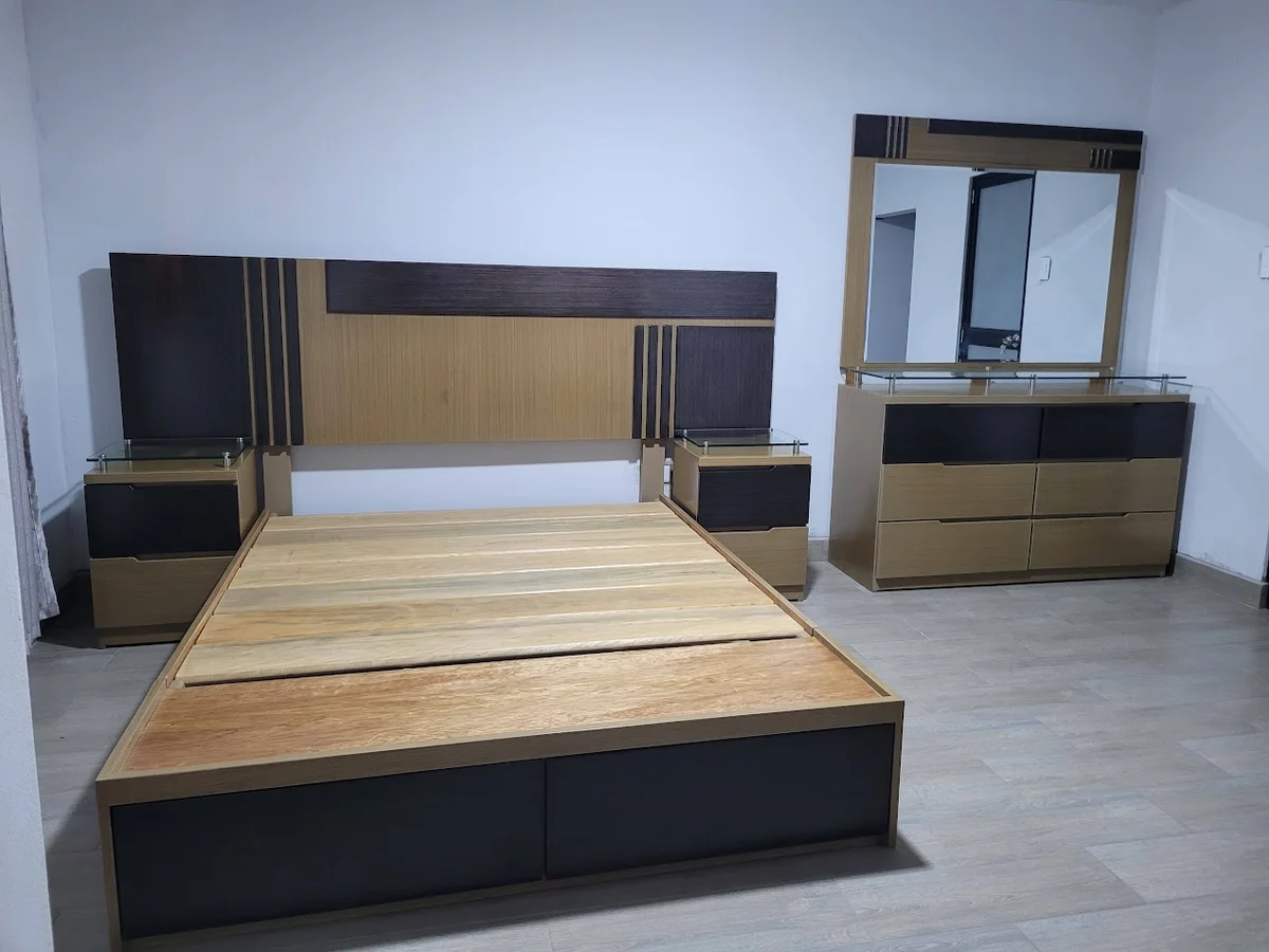 Juego de dormitorio del negocio con cama sin colchón, dos veladores y cómoda con espejo.